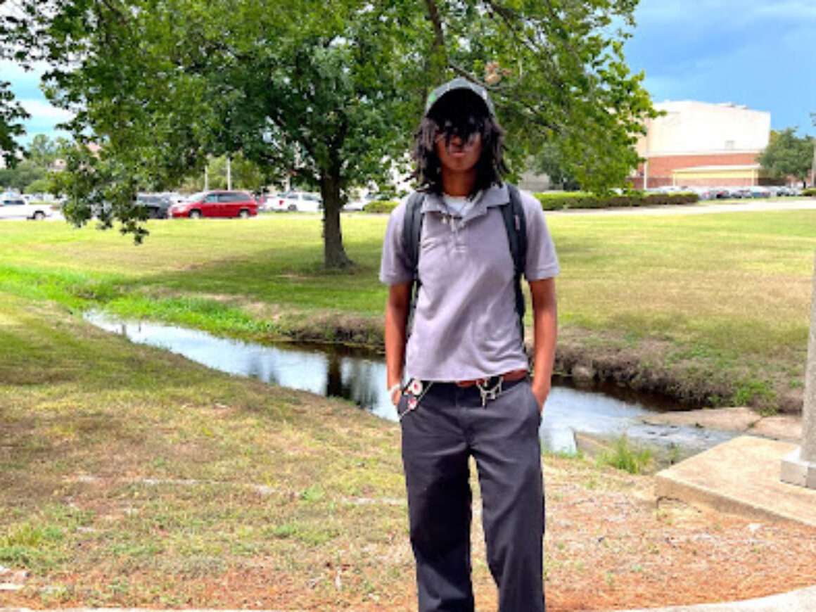 Student standing on sidewalk near water feature outside of campus student center.