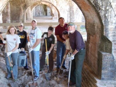 A group of students with shovels stand with a NPS officer