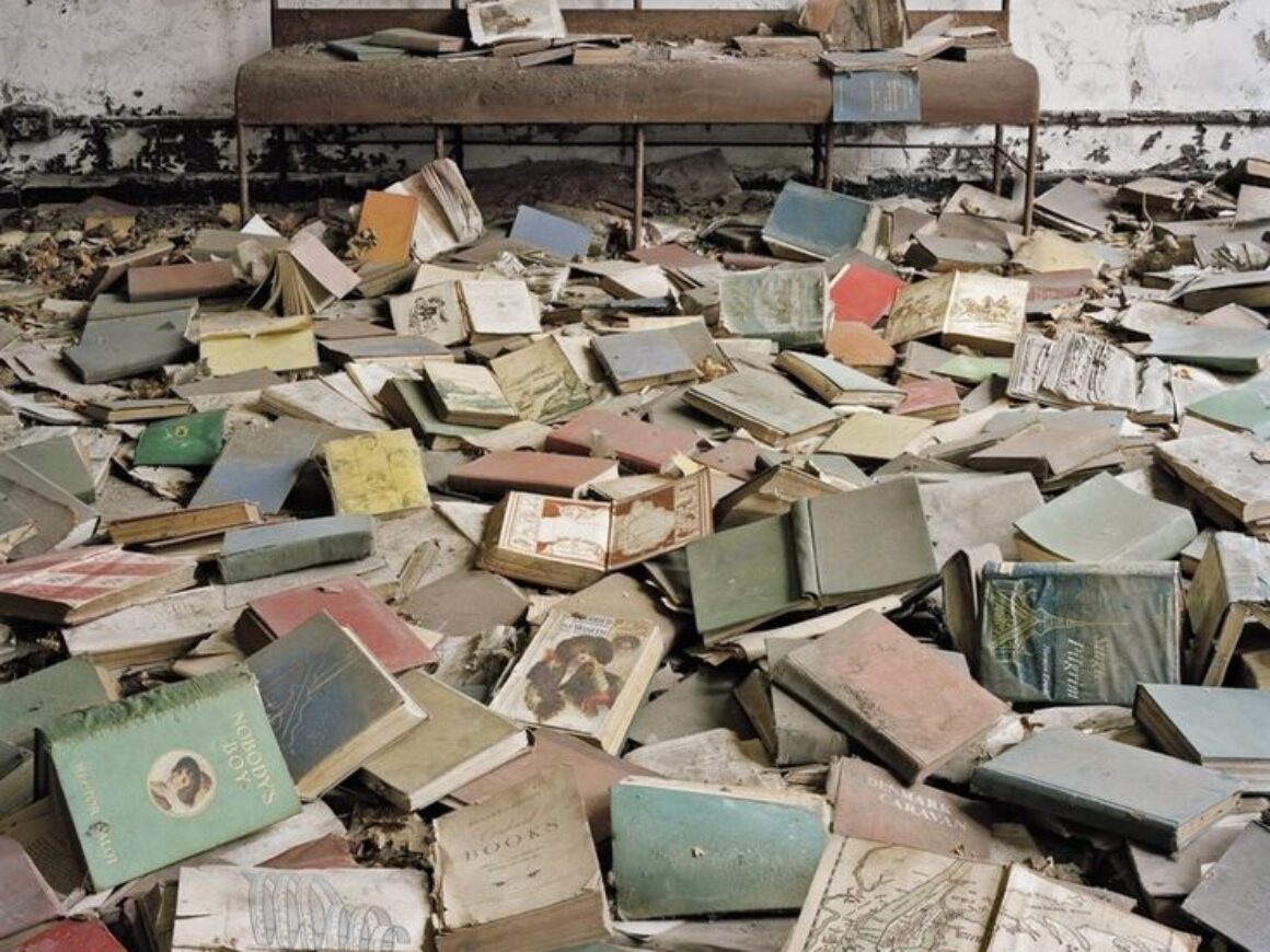 Many books piled on top of one another in a pile in front of a bench