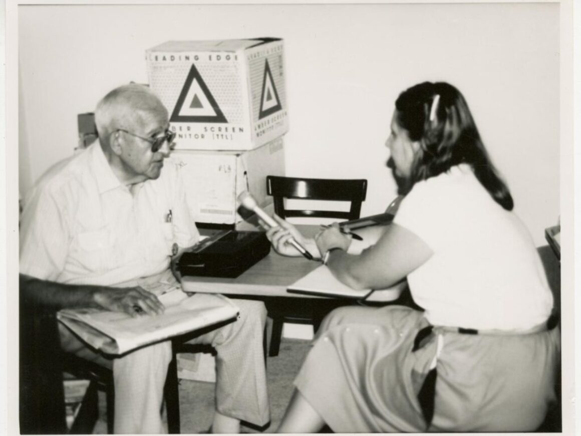 A woman holding a microphone interviews a man in 1990