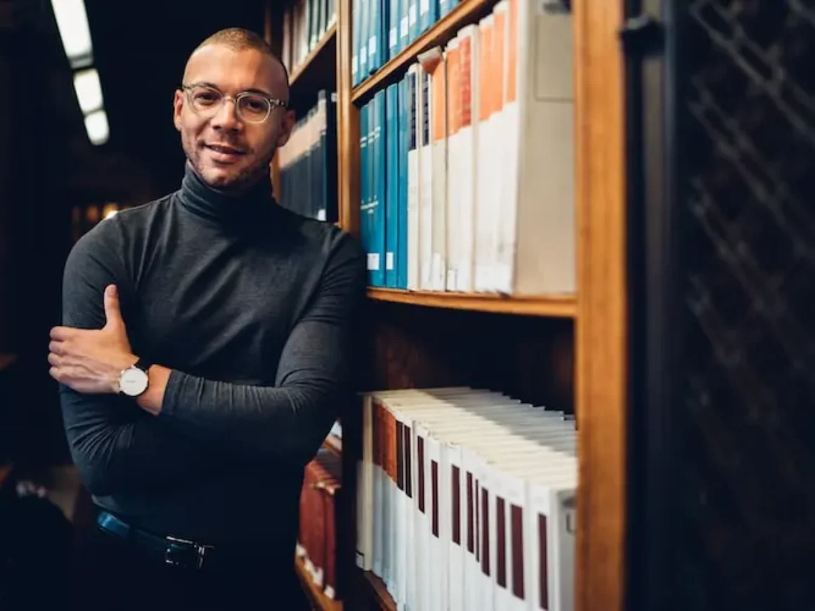 Man standing in a library stacks next to several books